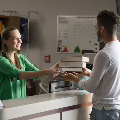 A female student worker hands books to another student at the AHU Library