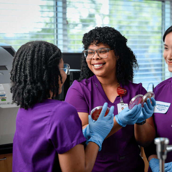 Three medical lab sciences students wearing scrubs practicing their skills using lab equipment.