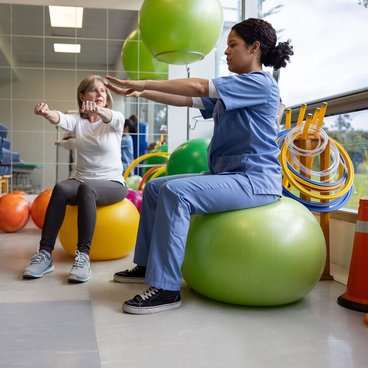 A female occupational therapist works with a patient using swiss exercise balls