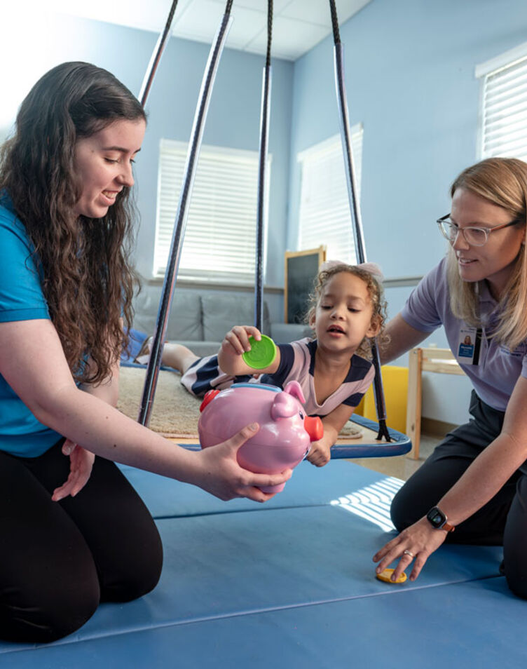 Image of faculty member smiling and helping pediatric patient with a student